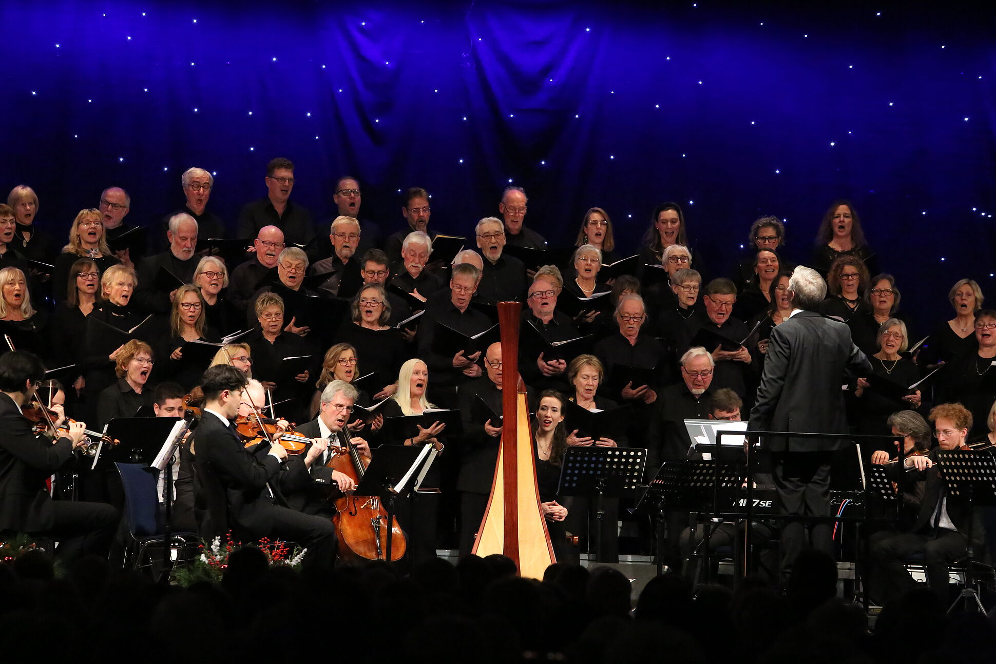 Der Konzertchor steht samt Dirigent auf der Bühne und alle sind festlich gekleidet. 