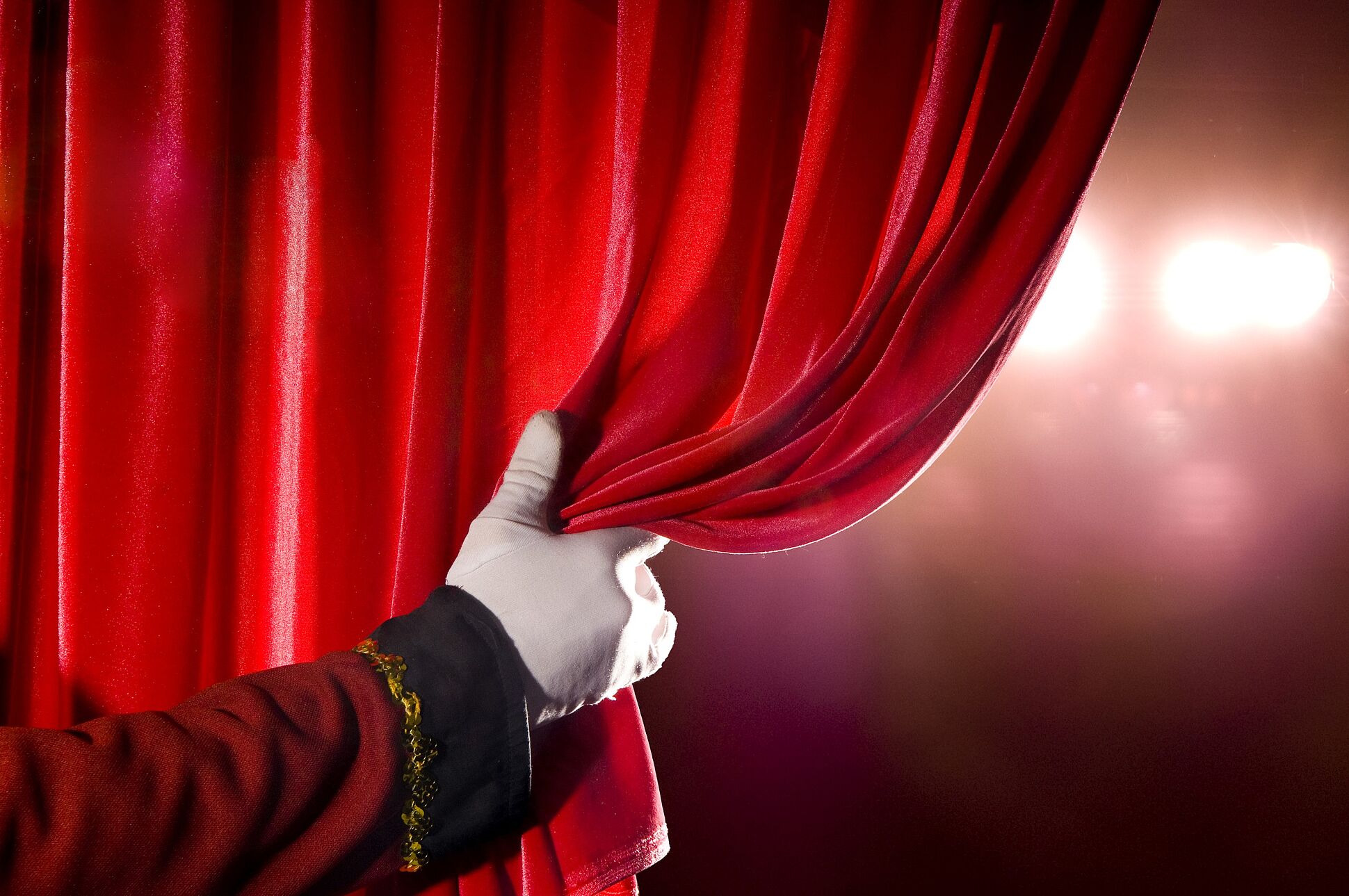 Eine Hand öffnet einen Vorhang eines Theaters.