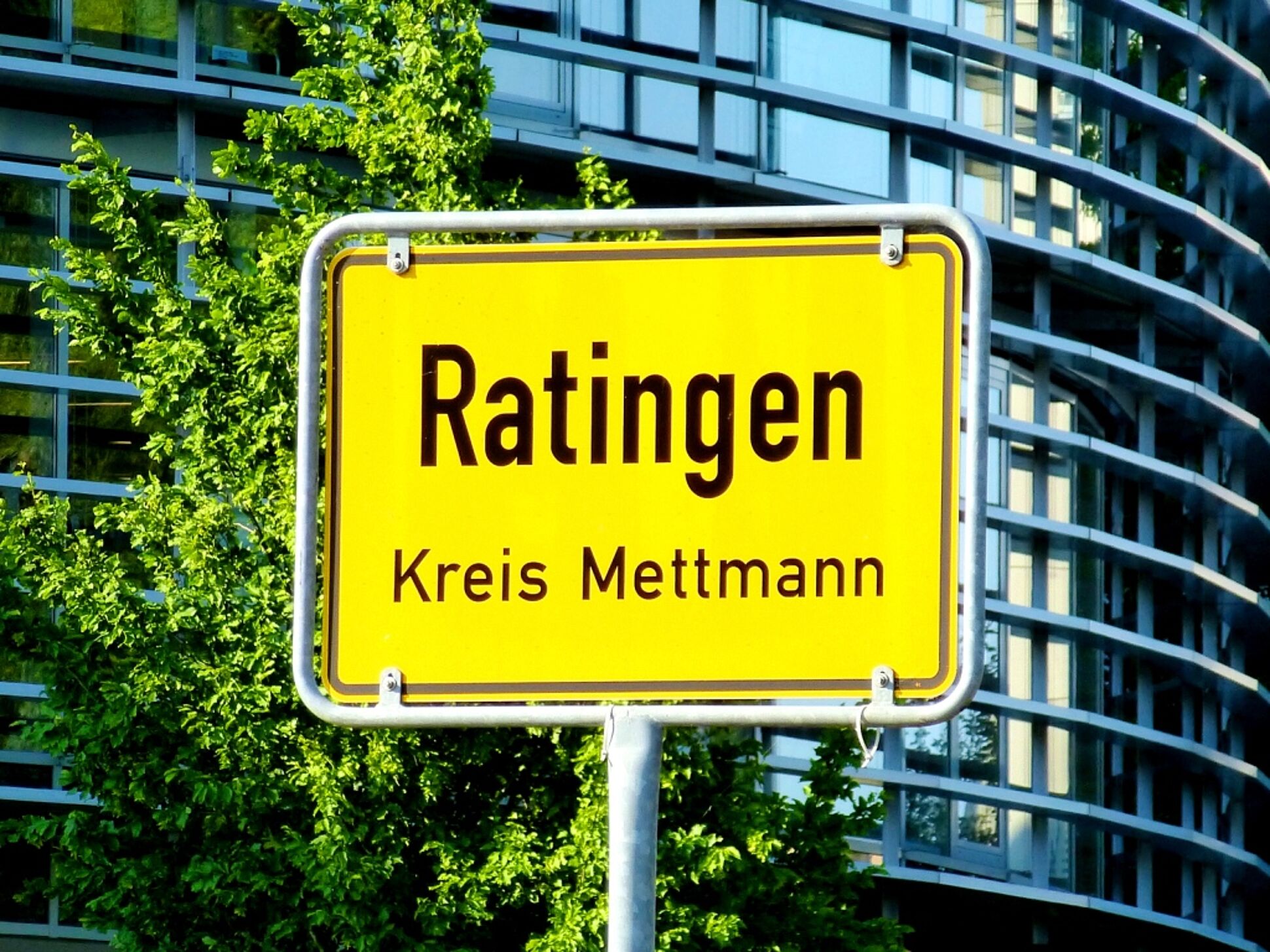 Ortseingangsschild der Stadt Ratingen vor einem modernen Bürogebäude